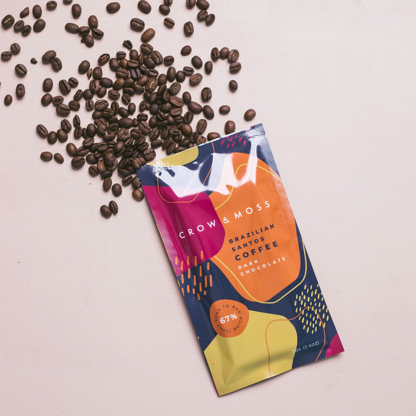 Scene depicting Brazilian Santos Coffee Dark Chocolate Bar 67% with coffee beans spilling over the table surface.