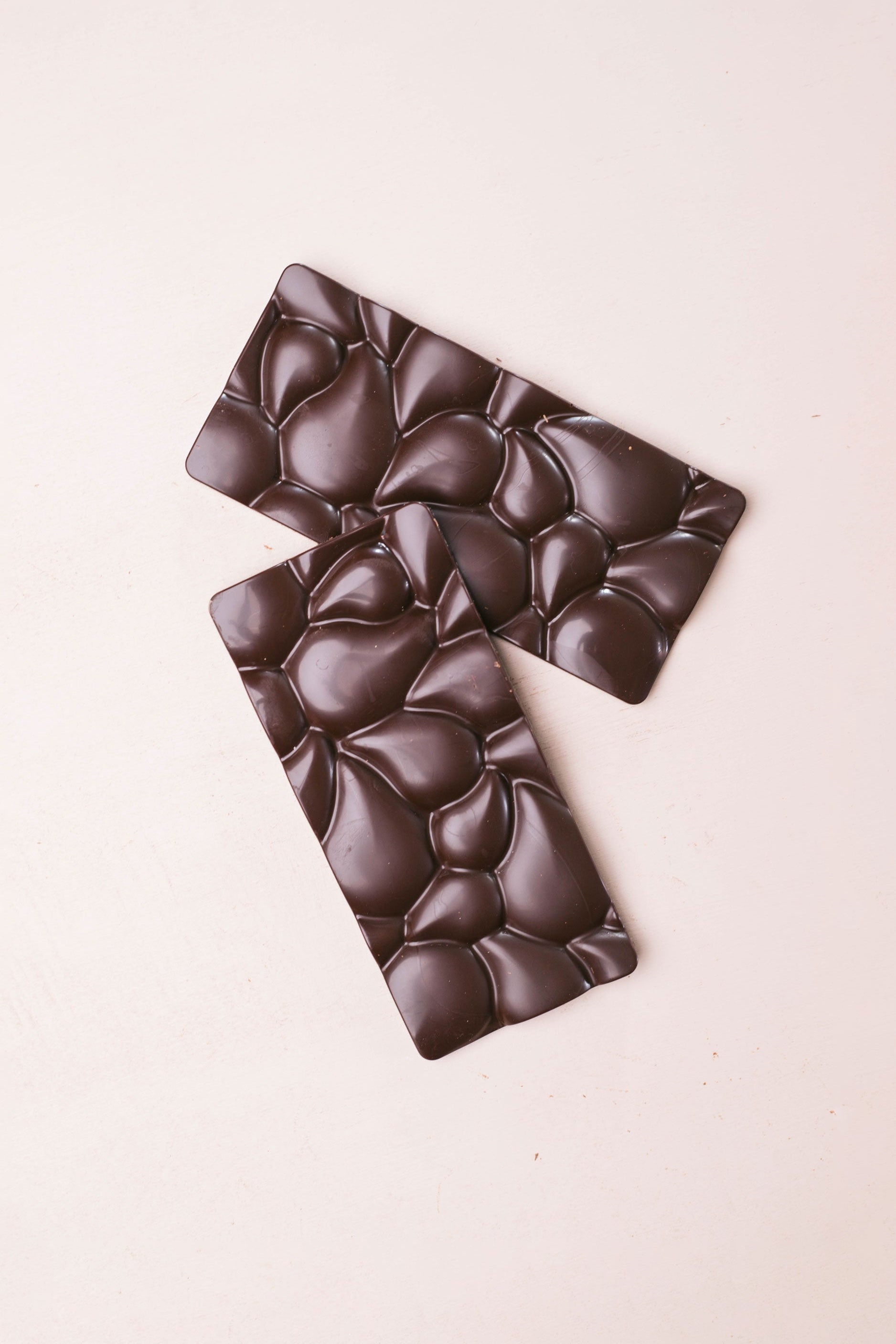 Dark chocolate bar with a textured surface on a light pink background